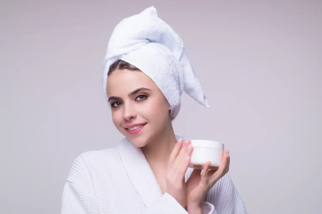 Fotografía minimalista de una mujer joven aplicando crema facial en un ambiente otoñal, con luz cálida natural, tonos tierra y un fondo desenfocado elegante. Estilo realista, profesional, revista de belleza.